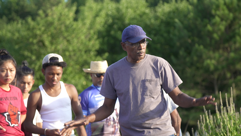 Farmer in a tshirt and ball cap explaining something to a group of young people