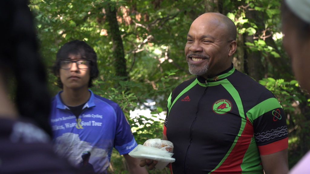 Kevin Hicks, Triangle Bikeworks leader, smiling in a group of young riders before the ride begins