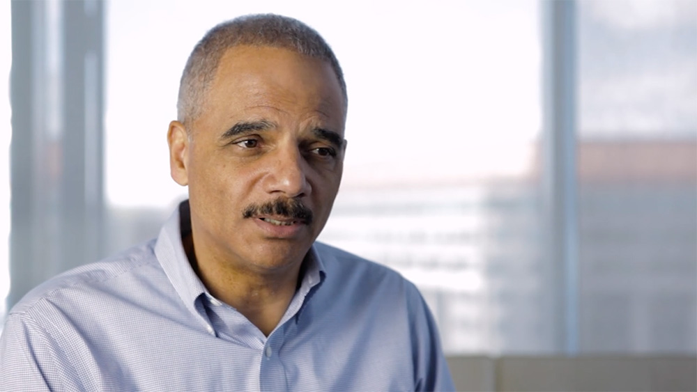 Eric Holder wearing a light blue button down in an interview about Janet Reno